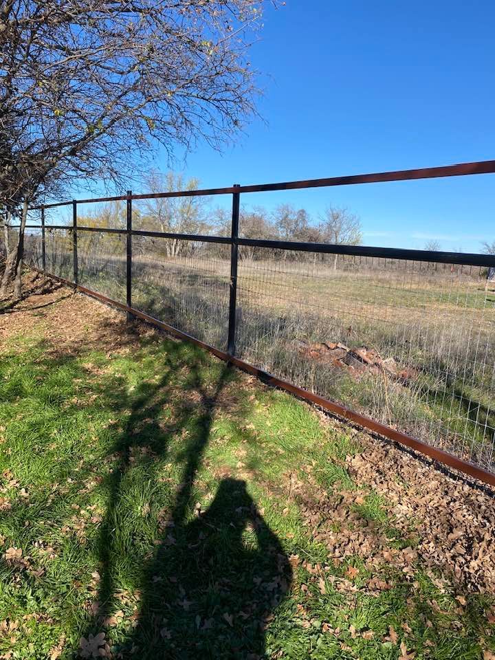 A person is taking a picture of a fence in a field.