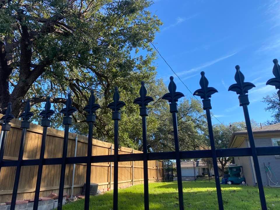 A wrought iron fence surrounds a backyard with a wooden fence.