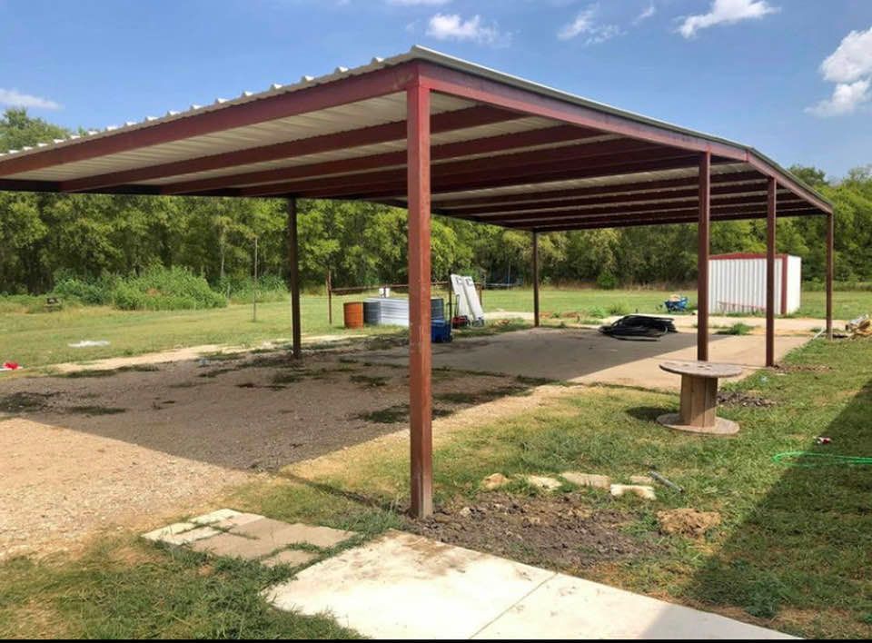 A metal carport is sitting in the middle of a grassy field.