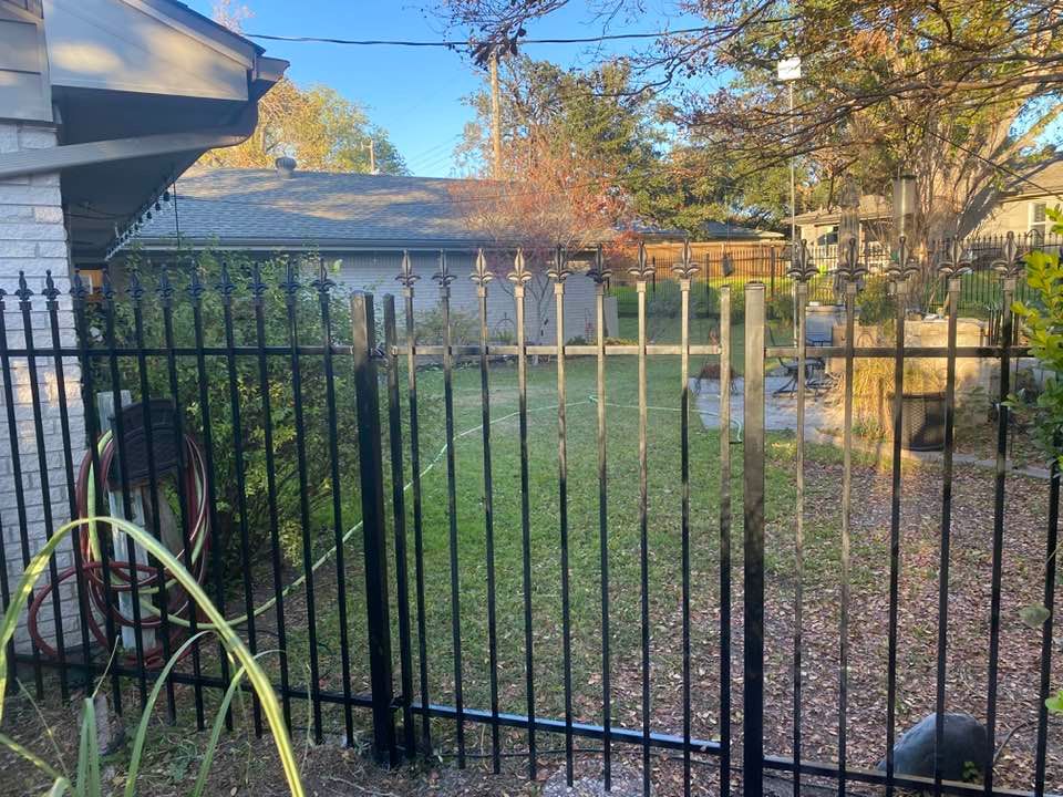 A black metal fence surrounds a yard with a house in the background.