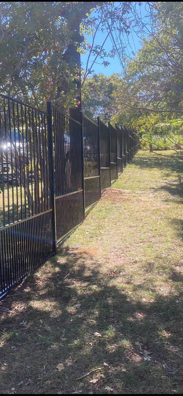 A metal fence surrounds a grassy field in a park.