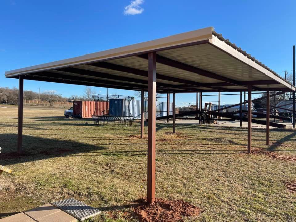 A metal carport is sitting in the middle of a grassy field.