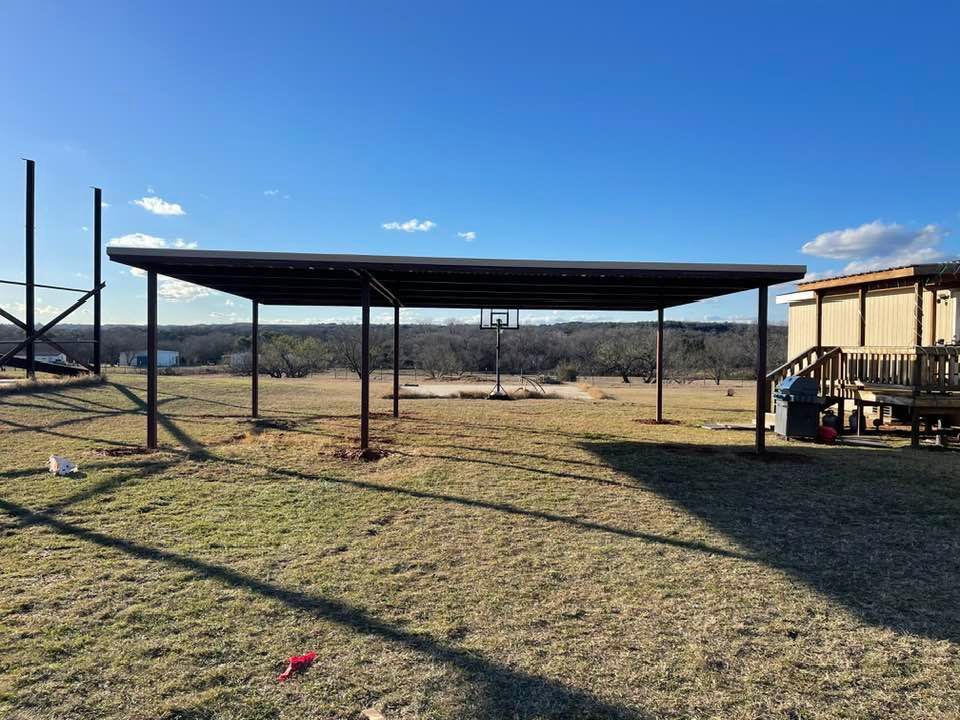 A carport is sitting in the middle of a grassy field next to a house.