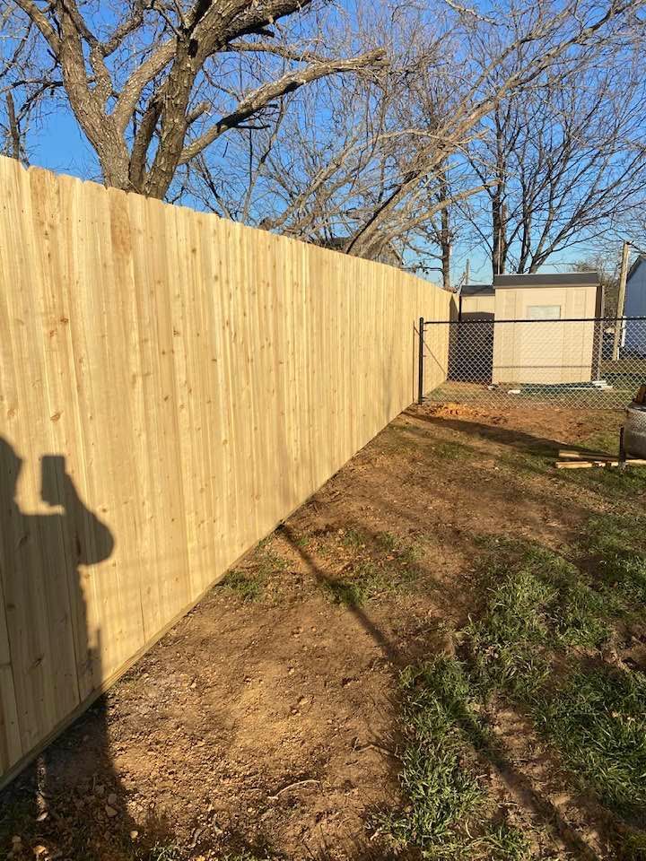 A wooden fence is surrounding a dirt path in a backyard.