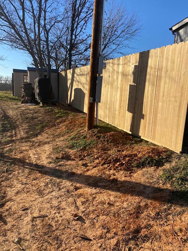 A wooden fence is sitting on the side of a dirt road next to a power pole.