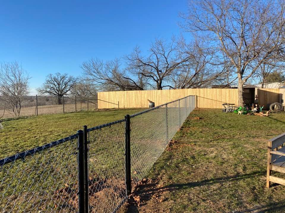 A chain link fence with a wooden fence behind it in a backyard.