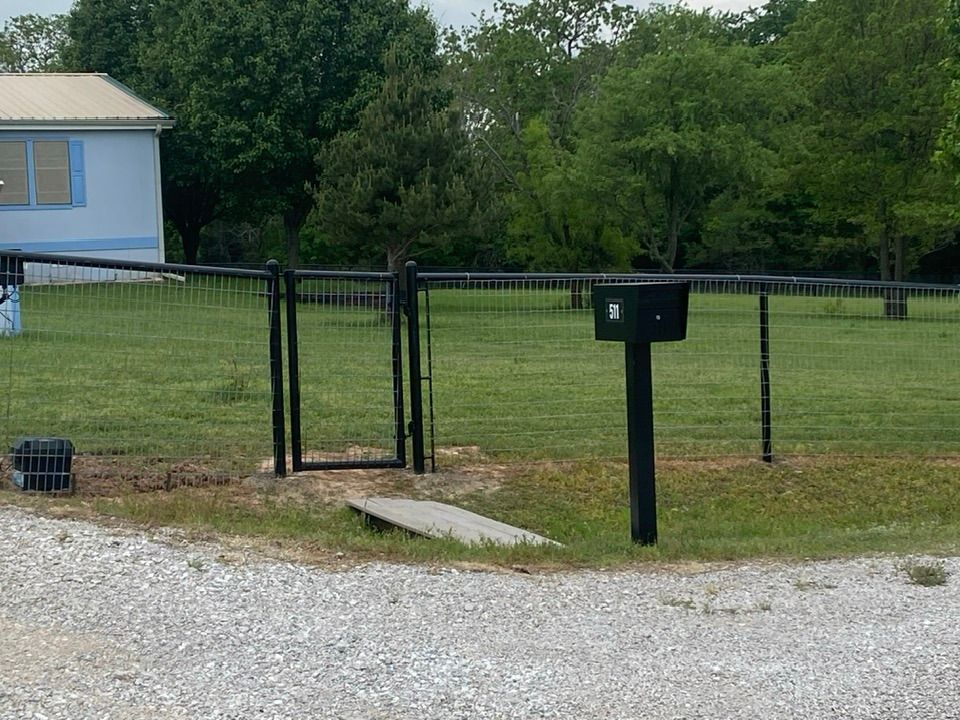 A mailbox in front of a fence with a house in the background
