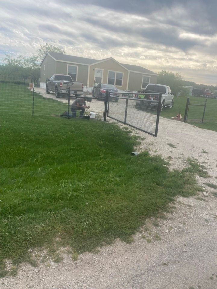A mobile home is sitting in the middle of a grassy field next to a fence.