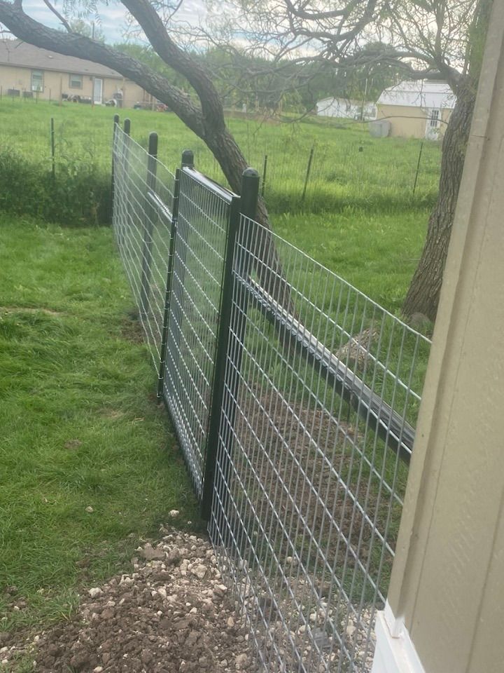 A fence is surrounding a grassy field next to a house.