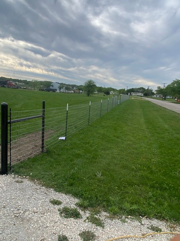 A fence surrounds a grassy field next to a gravel road.