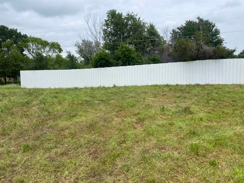 A white fence surrounds a grassy field with trees in the background.
