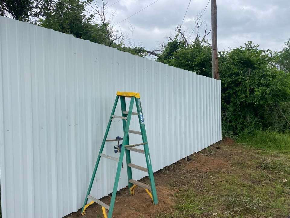 A green ladder is leaning against a white fence.