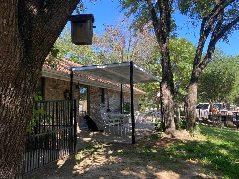 A house with a covered porch surrounded by trees and a birdhouse.