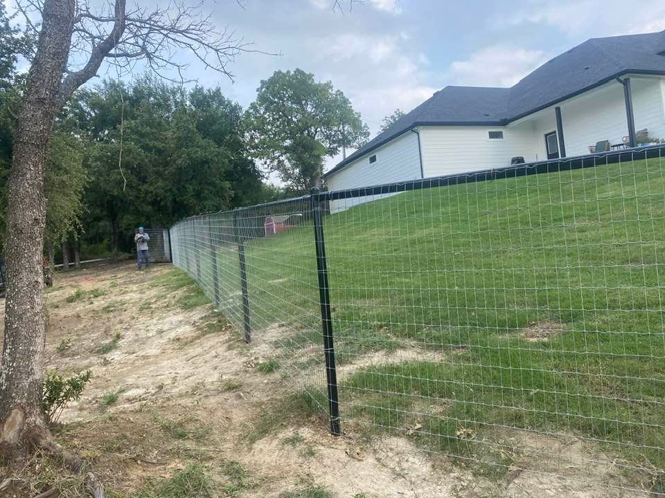 A fence is surrounding a grassy hill in front of a house.