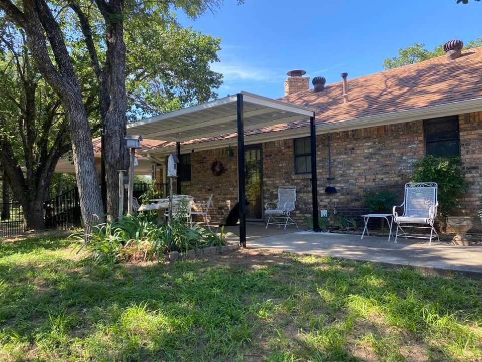 A brick house with a covered patio and chairs in front of it.