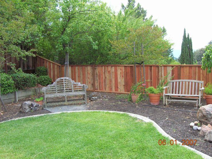 A wooden fence surrounds a lush green lawn in a backyard.