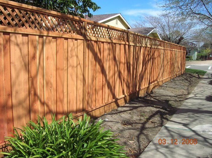A wooden fence with a lattice top is next to a sidewalk.