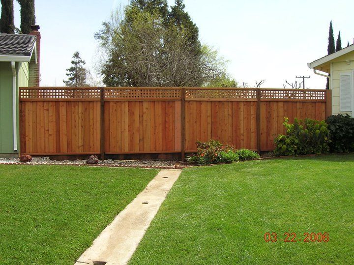 A wooden fence surrounds a lush green lawn in front of a house.