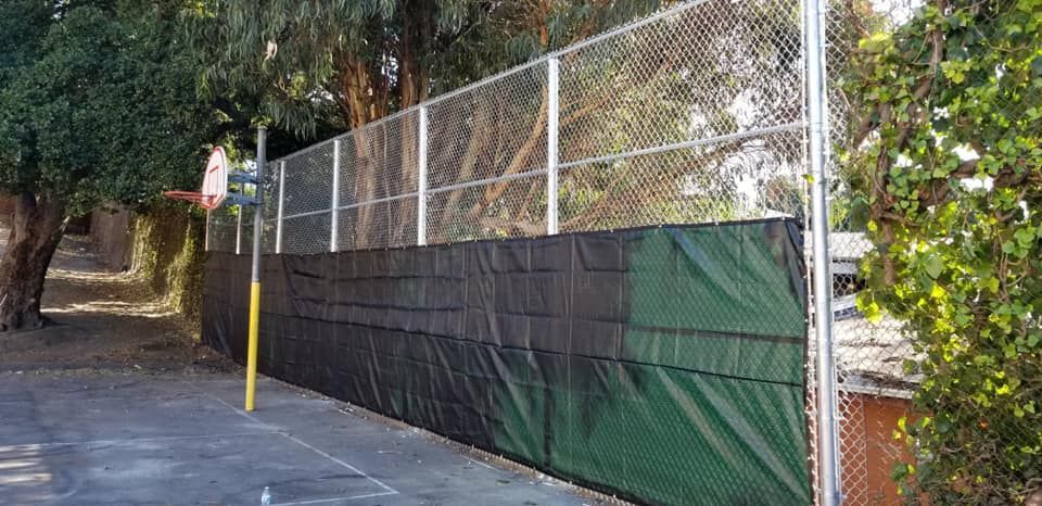 A fence with a green tarp on it is surrounded by trees.