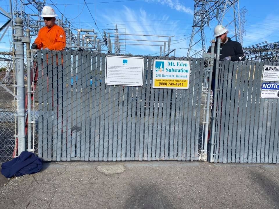 Two men are standing behind a fence with warning signs on it.