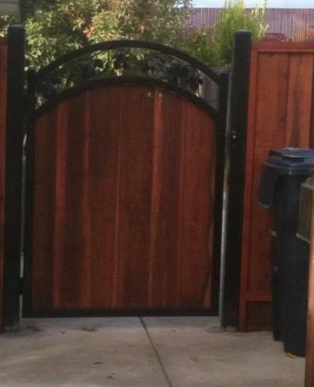 A wooden gate with a black frame is surrounded by trash cans.