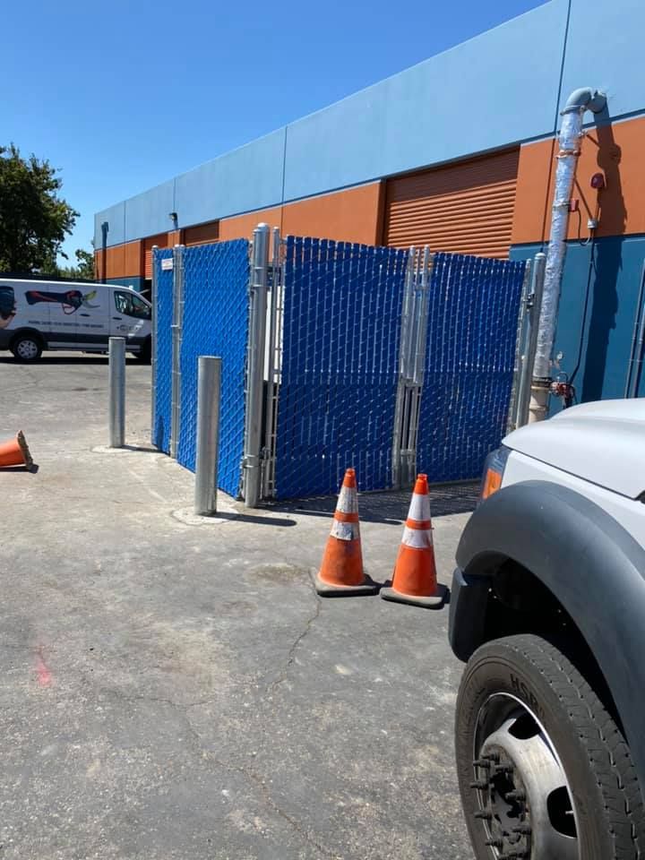 A white truck is parked in front of a blue fence and orange cones