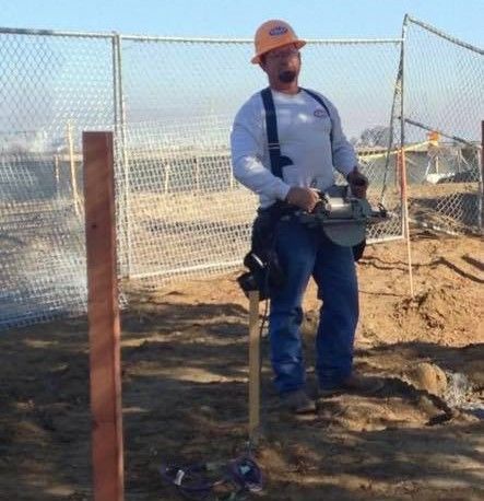 A man wearing a hard hat is standing in the dirt holding a saw