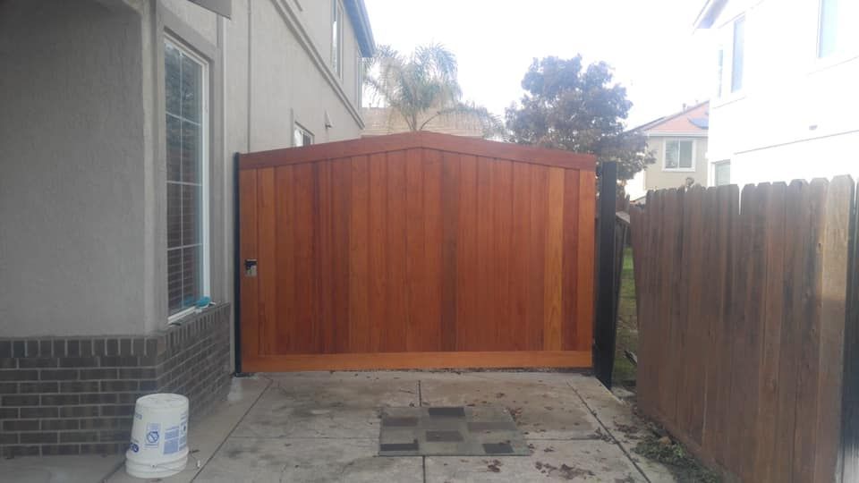 A wooden gate is sitting in front of a house next to a fence.