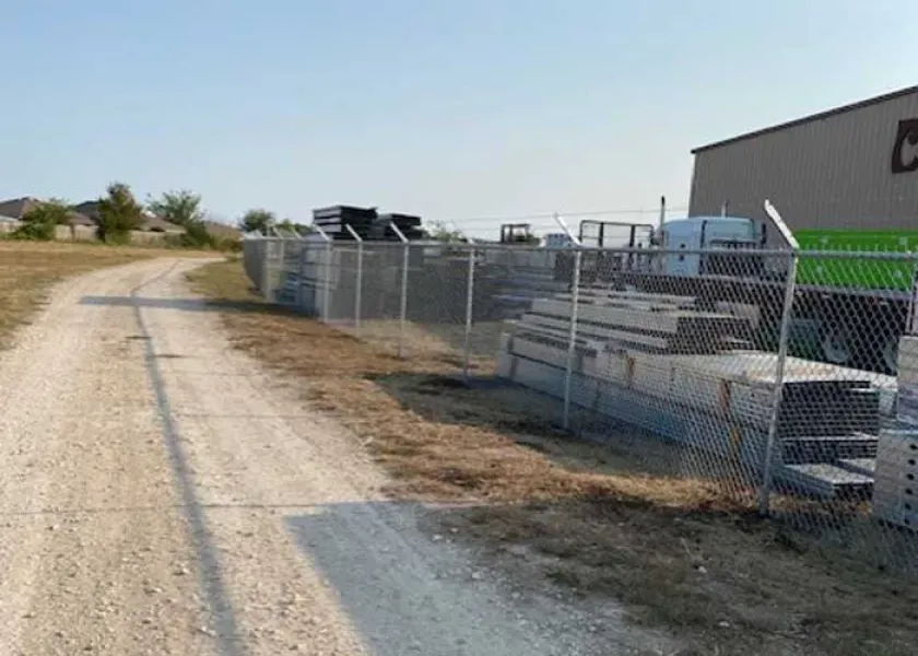 A chain link fence surrounds a dirt road leading to a building.