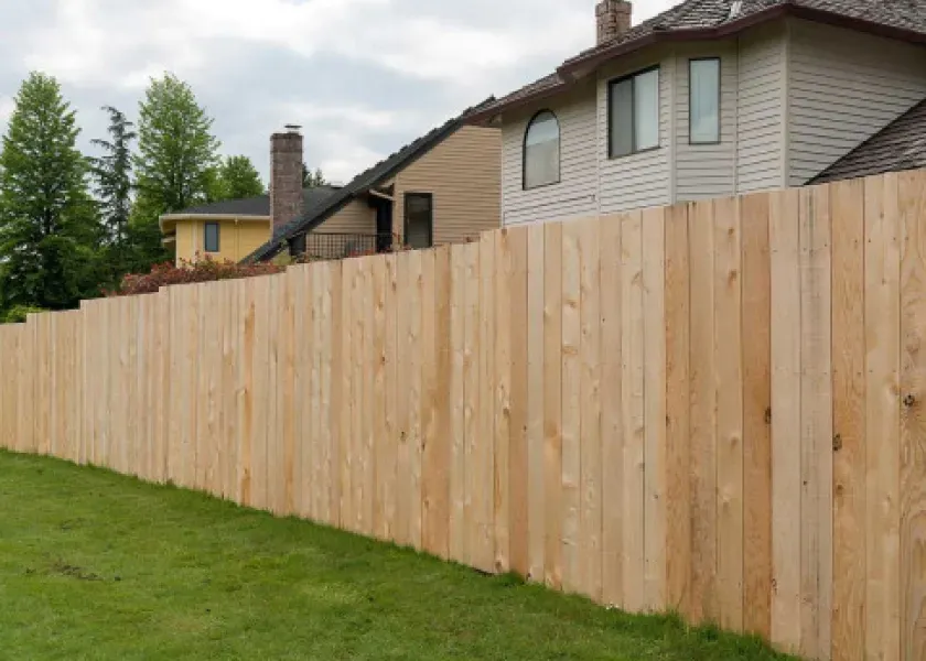 A wooden fence surrounds a lush green yard in front of a house.