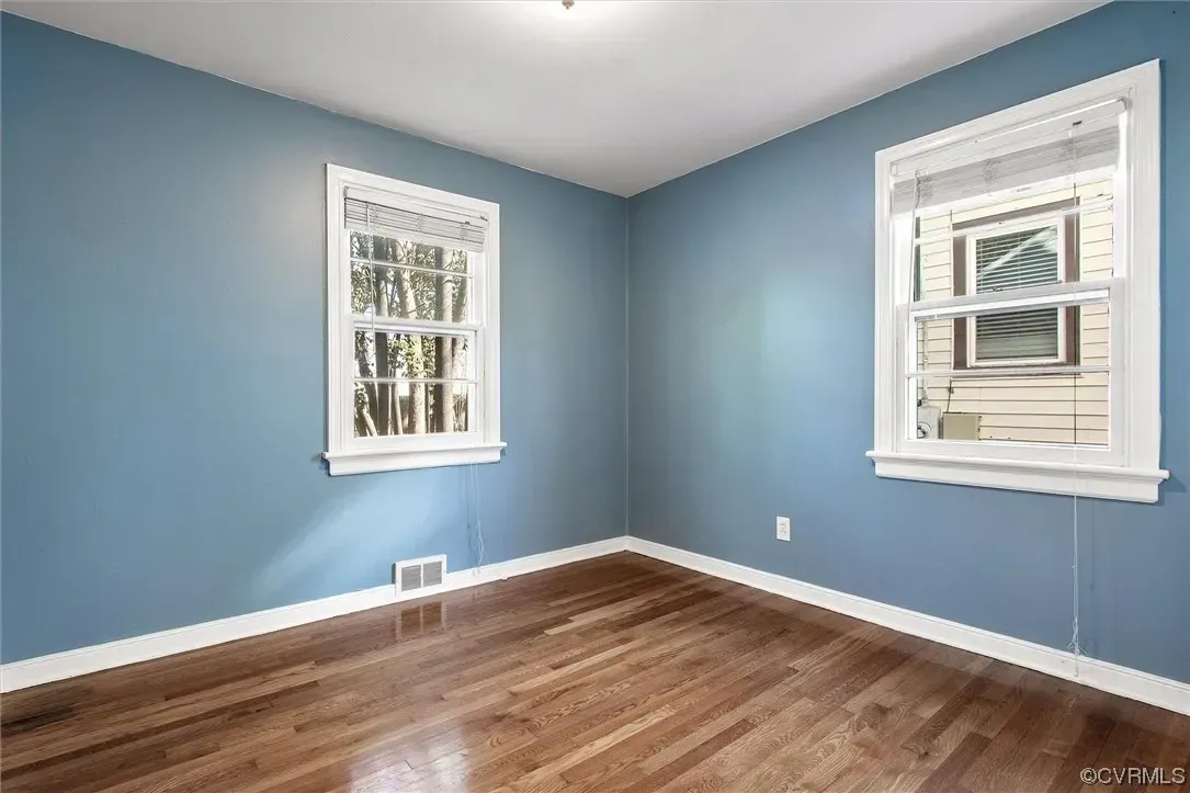 An empty room with blue walls and hardwood floors and two windows.