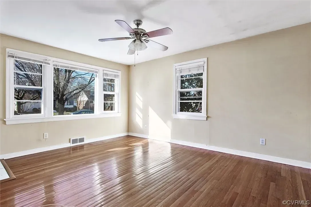 An empty living room with hardwood floors and a ceiling fan.