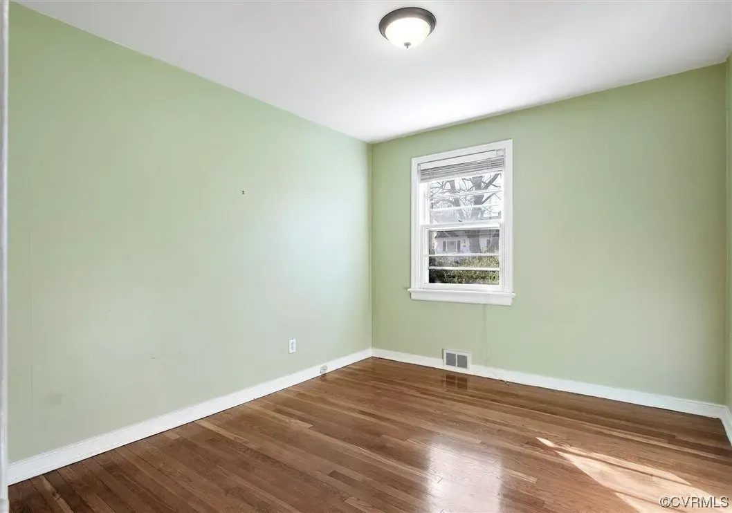 An empty room with green walls and hardwood floors and a window.