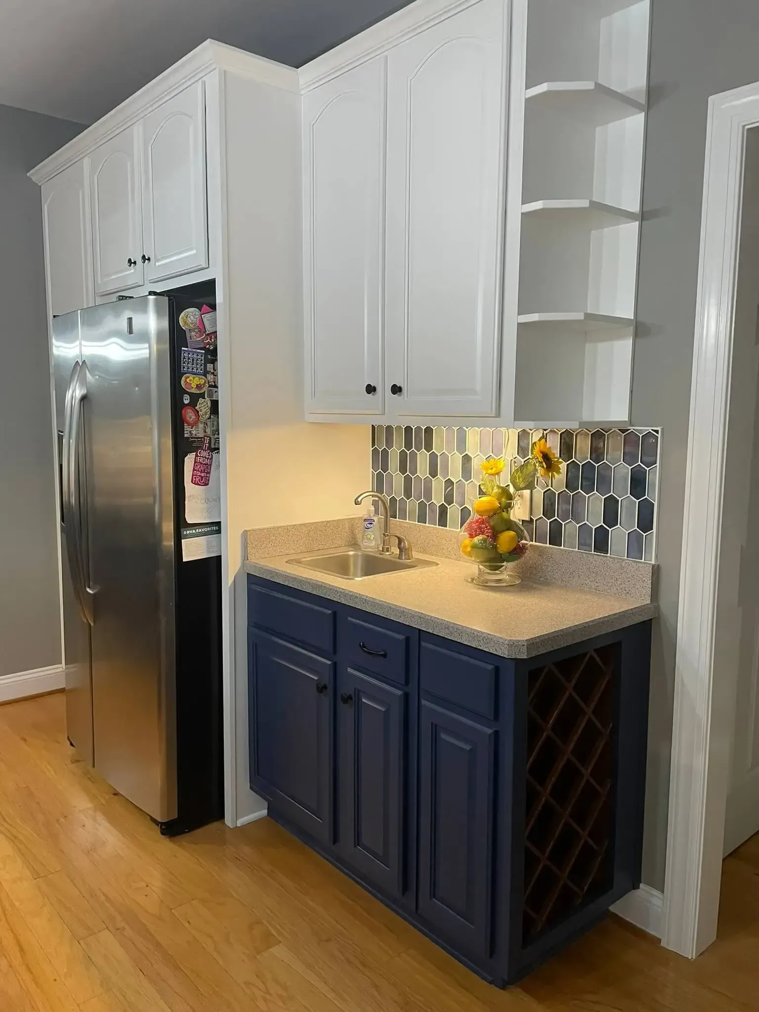 A kitchen with blue cabinets , white cabinets , stainless steel appliances and a wine rack.