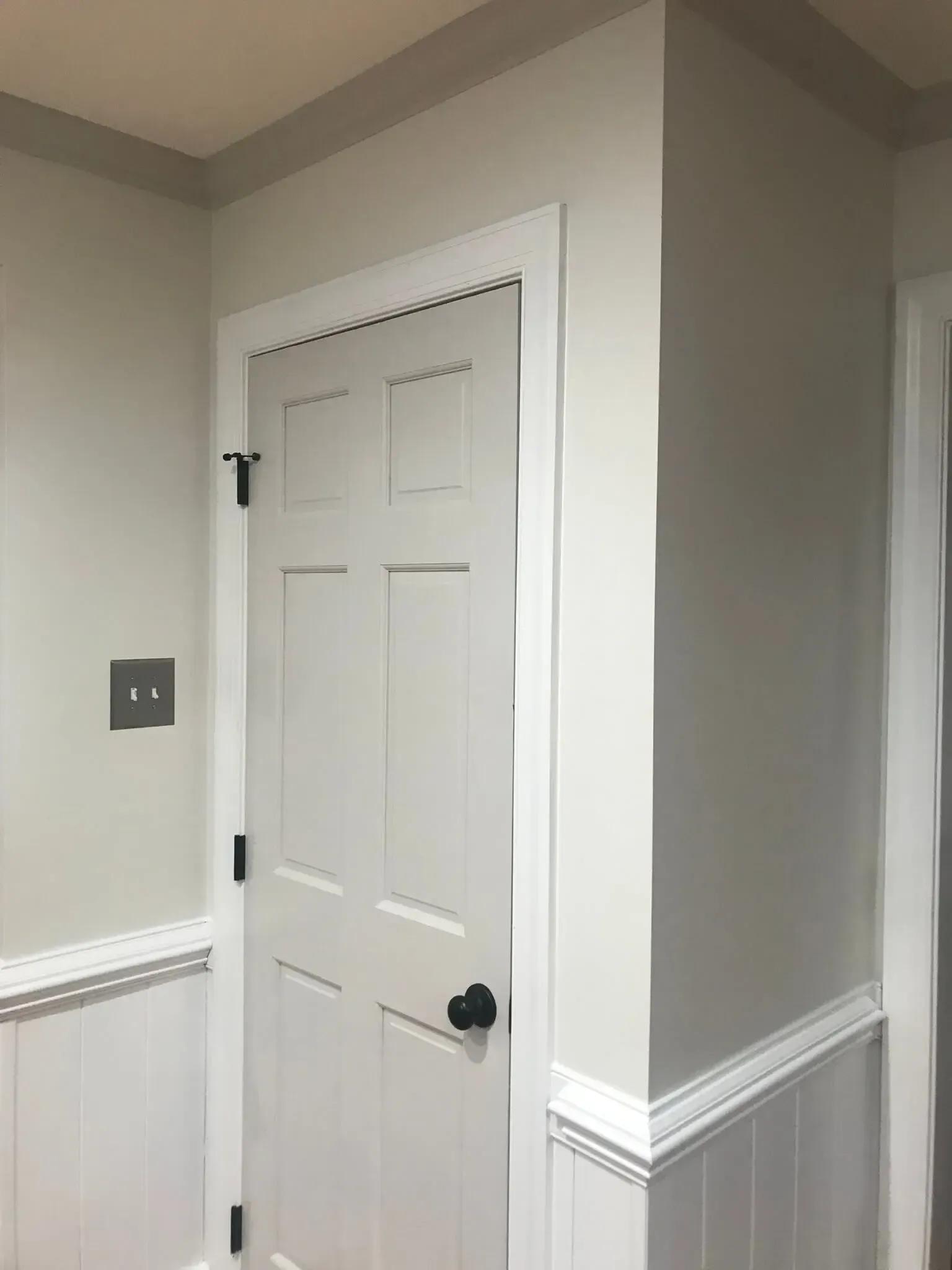 A white door with a black knob is in a hallway.