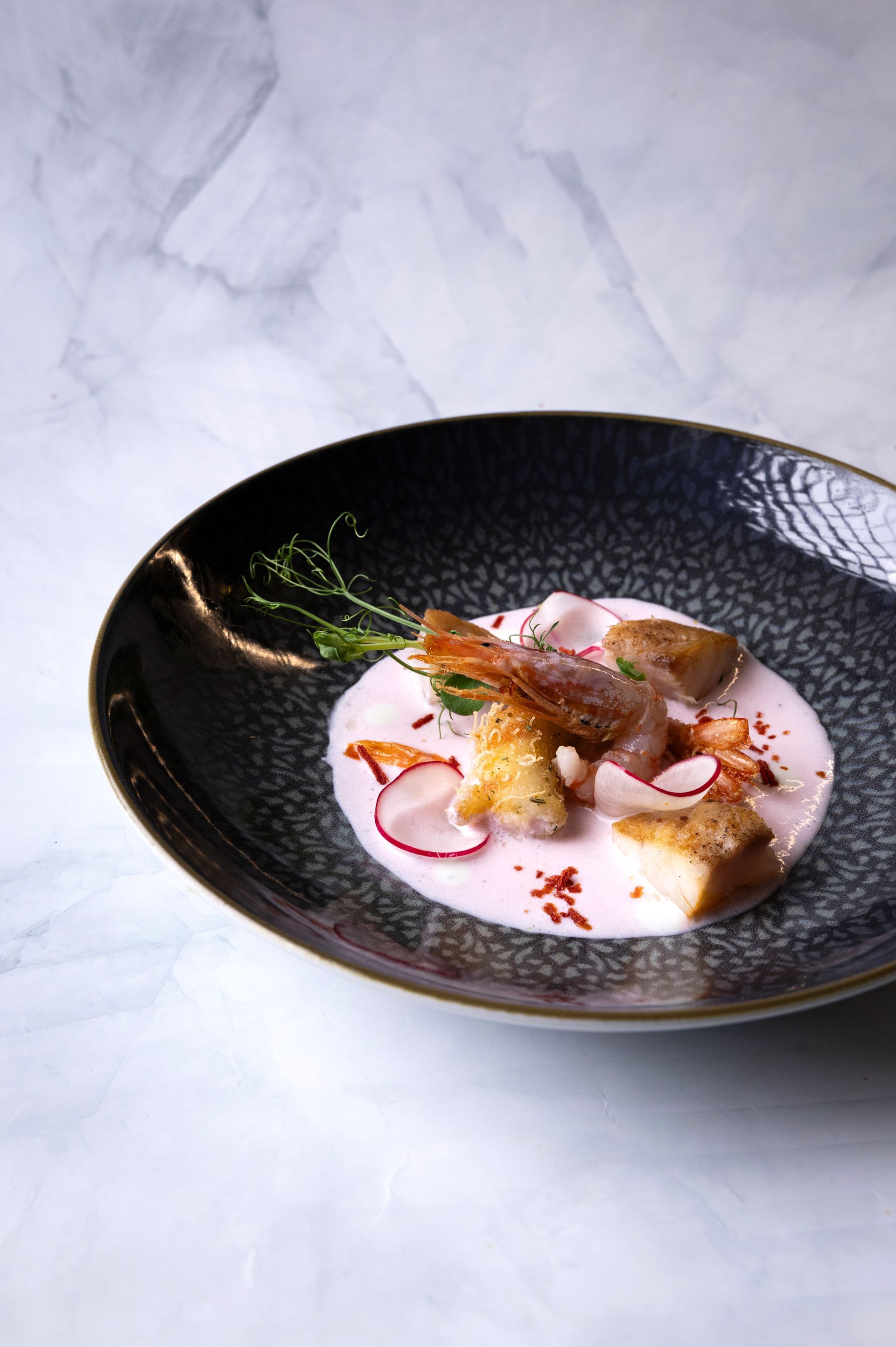 Un piatto di zuppa rosa con gamberi e crostini, guarnito con fette di ravanello ed erbe aromatiche.