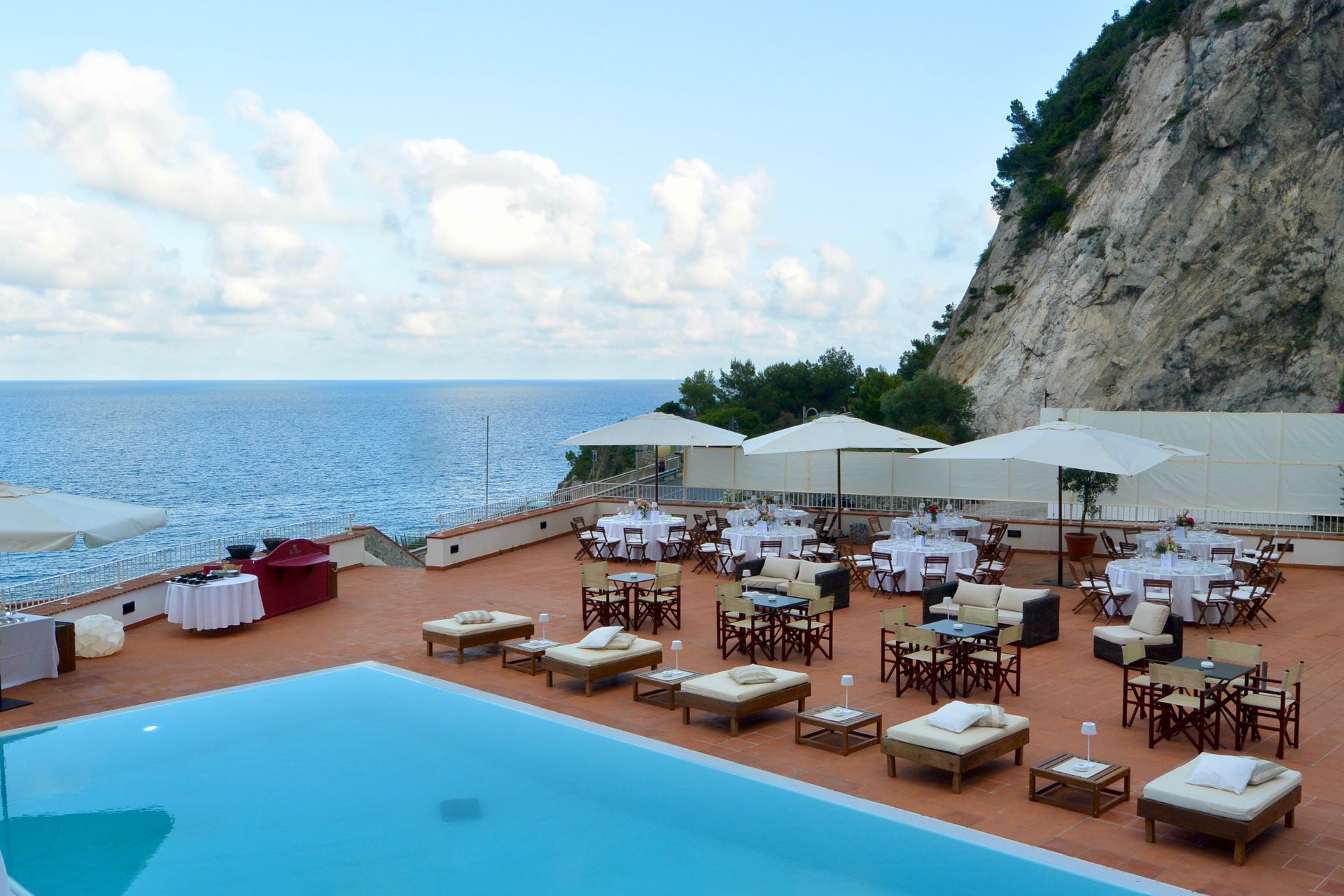Ristorante all'aperto e area lounge con vista sull'oceano, con piscina in primo piano. Tavoli e sedie sono predisposti per consumare i pasti.