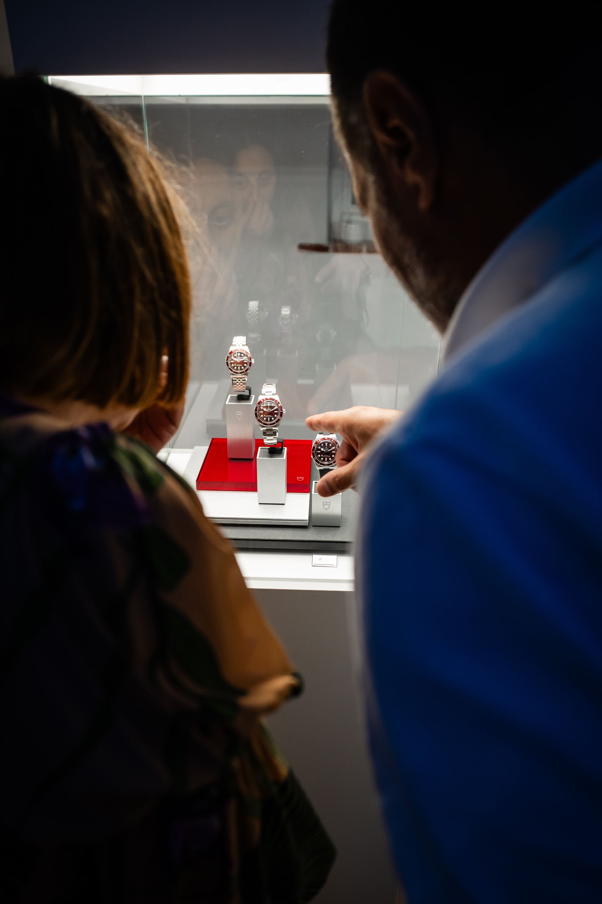 Un uomo e un bambino guardano gli orologi esposti in una vetrina illuminata. L'uomo indica un orologio.