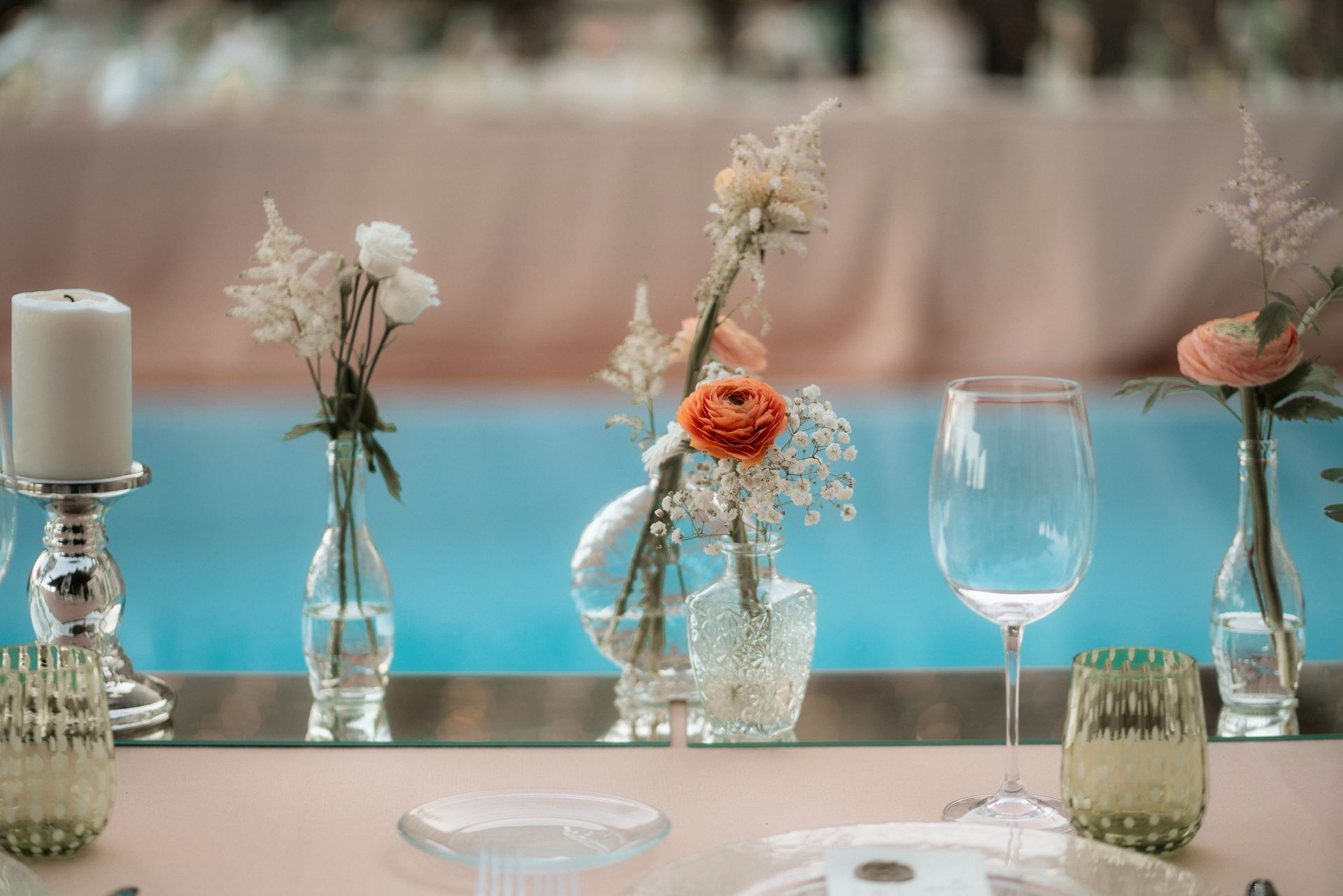 Un tavolo decorato con centrotavola floreali, bicchieri e candele, su uno sfondo sfocato rosa e blu.