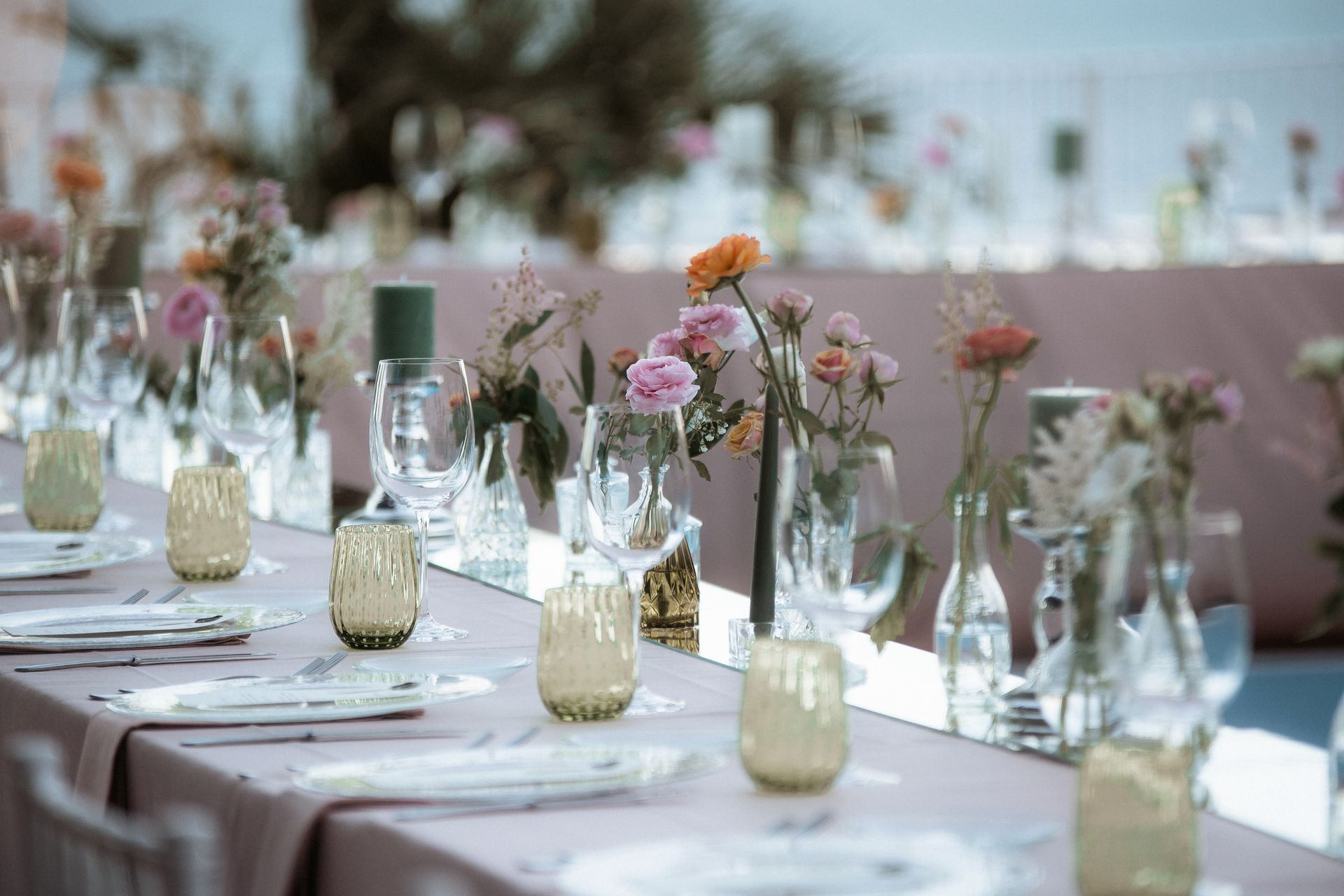 Lunga tavola apparecchiata per una festa con composizioni floreali, candele e tovaglie. Tovaglia rosa tenue con sfondo sfocato.