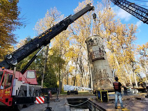 A man is standing next to a crane lifting a large object.
