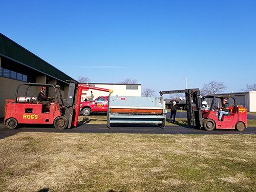 Two forklifts are moving a large piece of metal in a field.