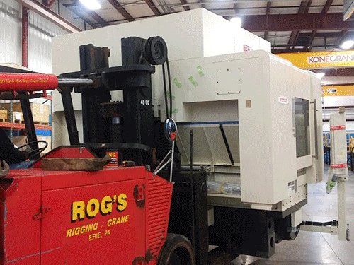 A large machine is being lifted by a forklift from rog 's rigging crane