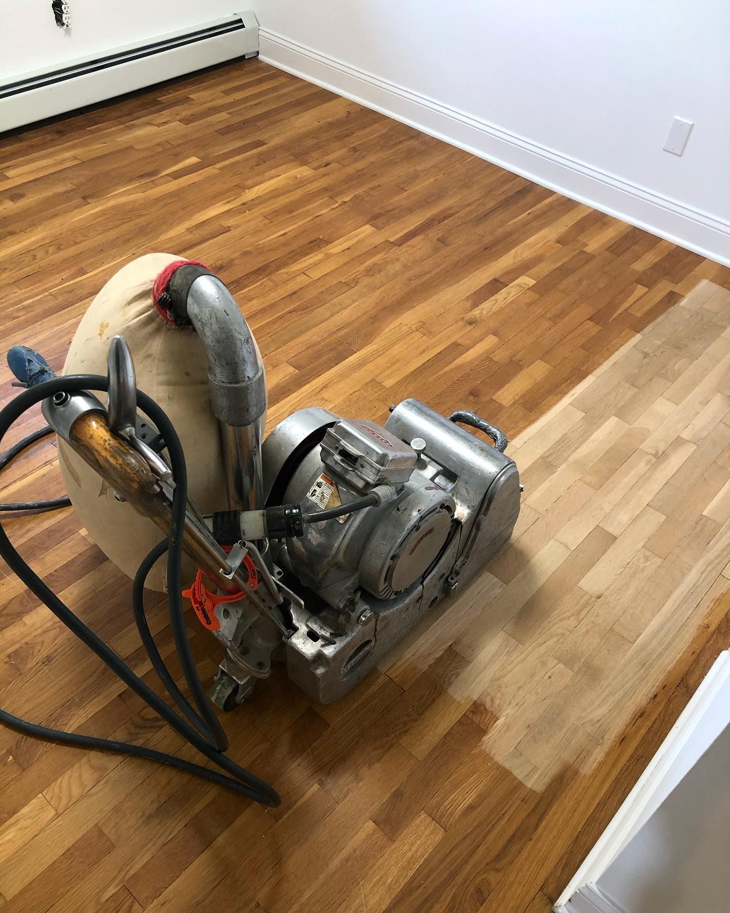 Floor sander on hardwood floor, sanding half the room.