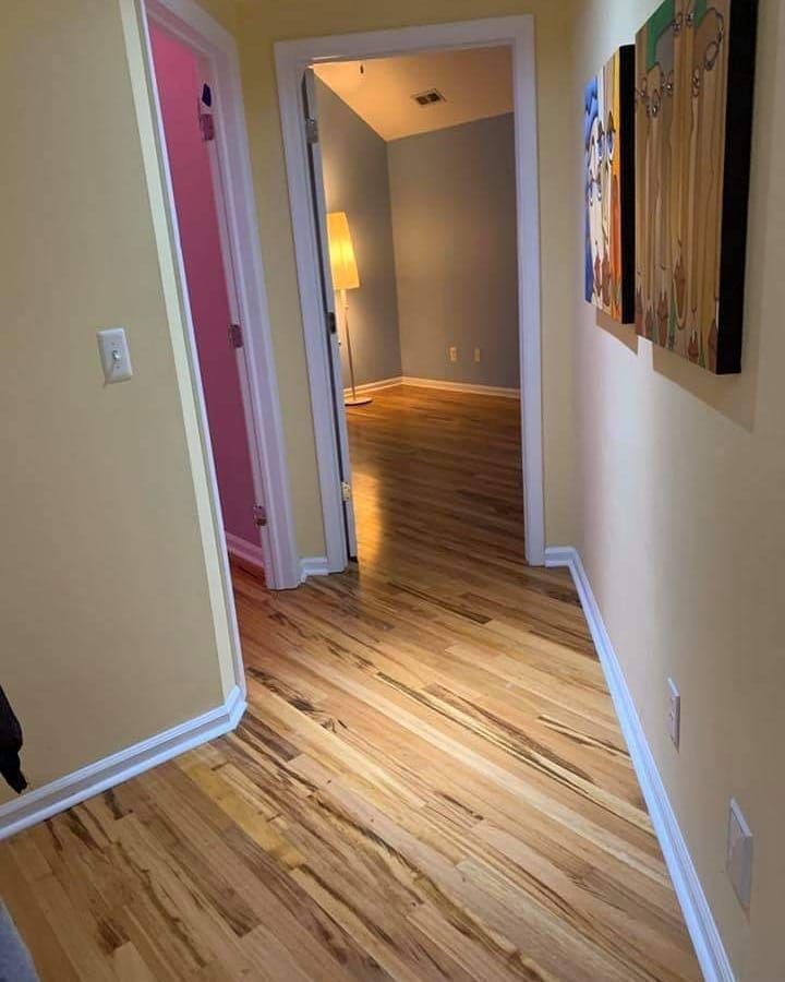 Hallway with hardwood floors, leading to rooms with different colored walls; art on the right wall.