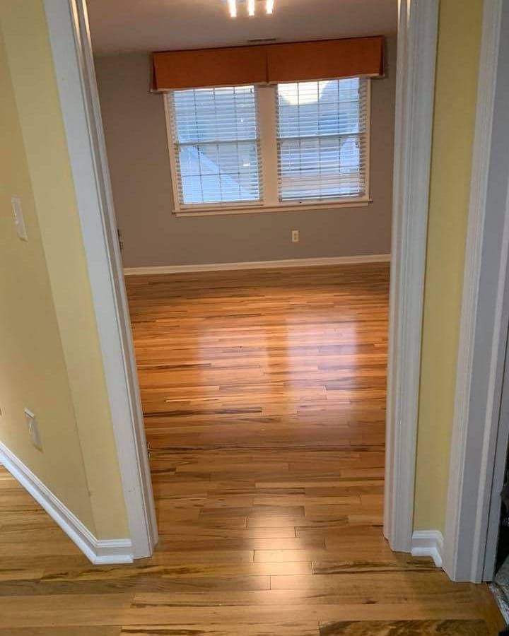 View into a room with wood floors, a window, gray walls, and orange valance, framed by a doorway with 