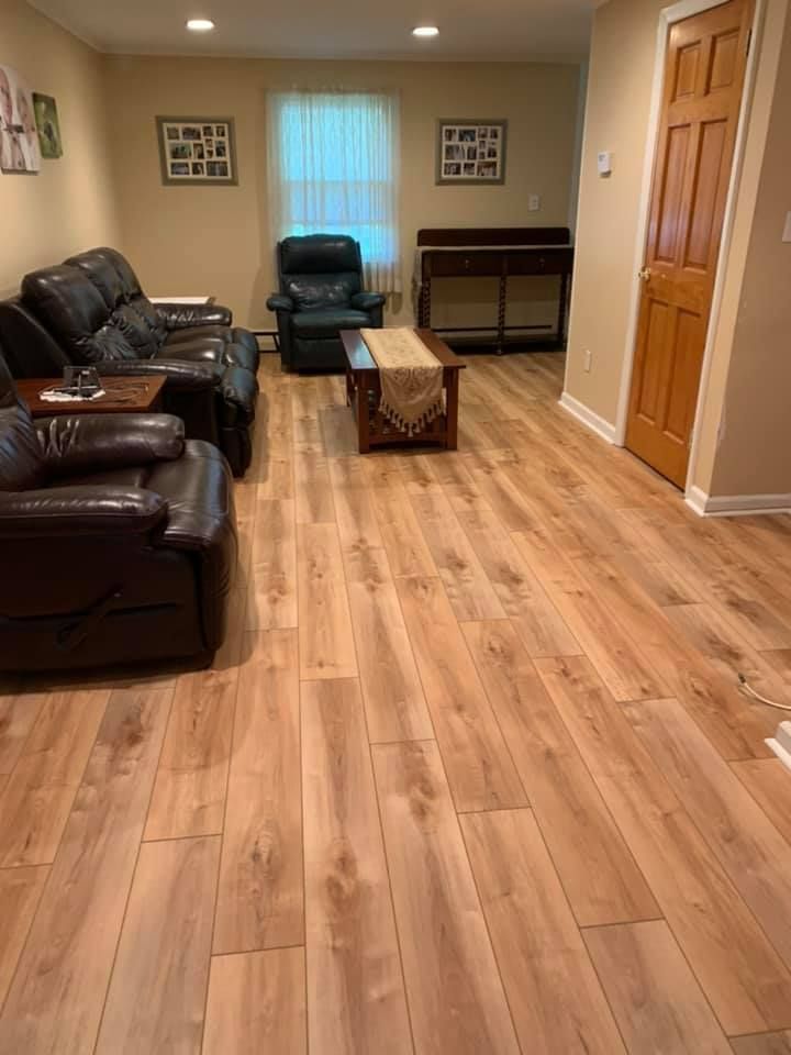 Living room with light wood floor, dark leather furniture, a piano, and a window.