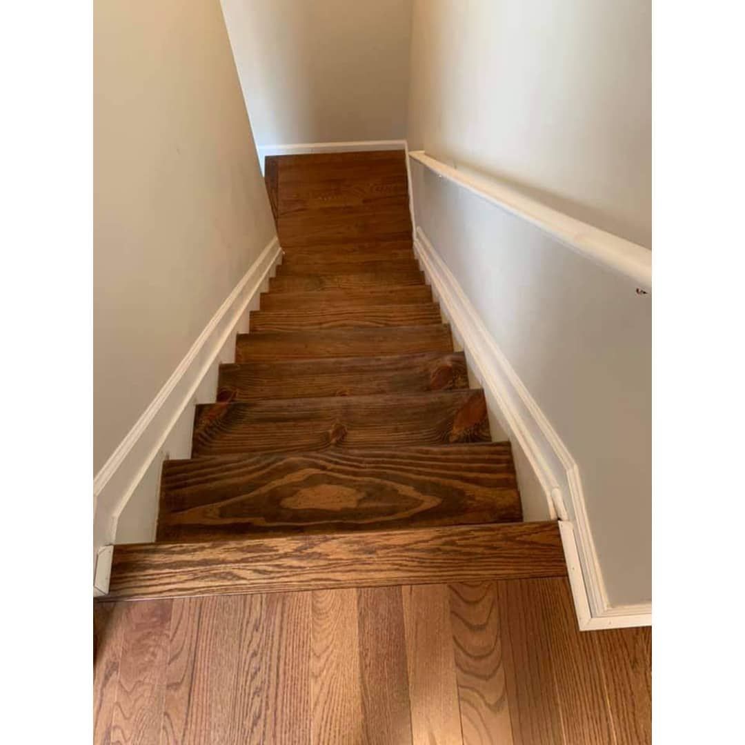 Wooden staircase with white trim and a handrail, leading down from a landing.