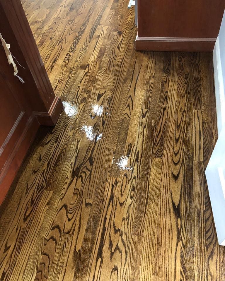 Wooden floor with light-colored splotches between two cabinets.