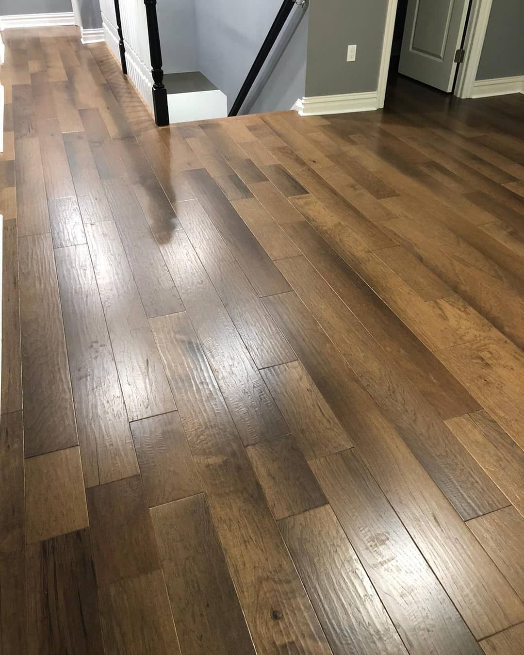 Wood flooring in a room with a staircase and a doorway. Brown planks with a glossy finish.